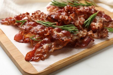Slices of tasty fried bacon with rosemary on white table, closeup