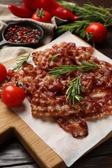 Slices of tasty fried bacon, rosemary, tomatoes and peppercorns on wooden table