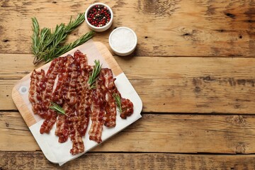 Slices of tasty fried bacon, rosemary, salt and peppercorns on wooden table, top view. Space for text