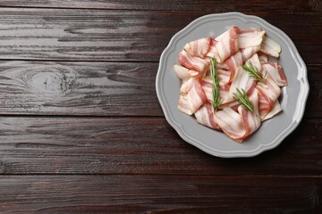 Slices of raw bacon and rosemary on dark wooden table, top view. Space for text