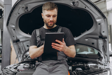 Happy mechanic using digital tablet at auto repair shop