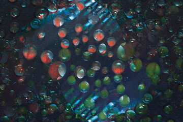 Green and red raindrops are illuminated by a flash of blue light and are located against a black-blue background. Abstract fantasy. 3D render.