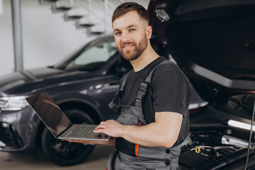 Mechanic man mechanic manager worker using a laptop computer checking car in workshop at auto car...
