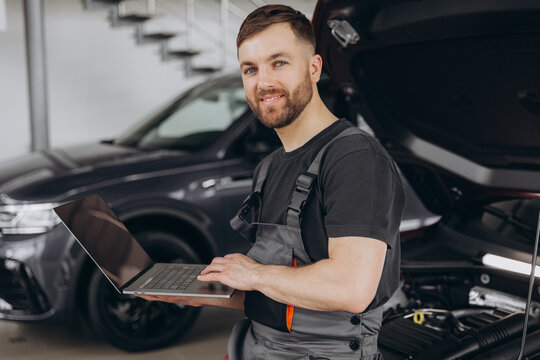 Mechanic man mechanic manager worker using a laptop computer checking car in workshop at auto car repair service center. Engineer young man looking at inspection vehicle details under car hood.