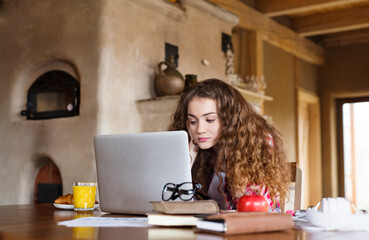 A beautiful university student is writing her thesis on a laptop, sitting at home on the couch.