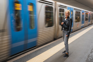 A girl of European appearance is standing in the subway and a train passes by.