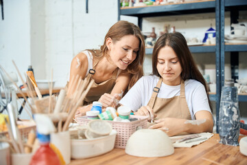 Woman potter painting handmade ceramic bowl with her teacher