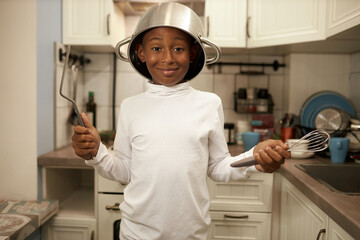 Portrait of black boy kid in blank mockup long-sleeve standing with cooking pan on head and whisk...