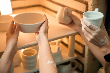 Unrecognizable women potters placing clay ceramics mugs kiln