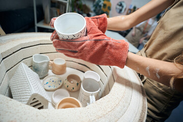 Unrecognizable female artisan taking glazed mug from kiln