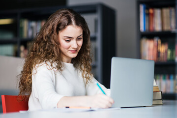 Young female student in library, focusing on final project, presentation, working on laptop....