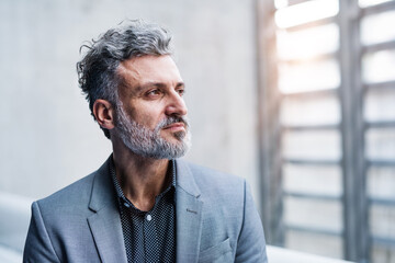 Portrait of handsome businessman standing in modern office hallway.