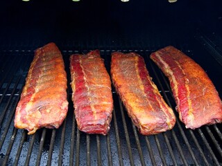 Smoking pork side ribs on a pellet grill; four racks of ribs in a grill after being smoked for two hours