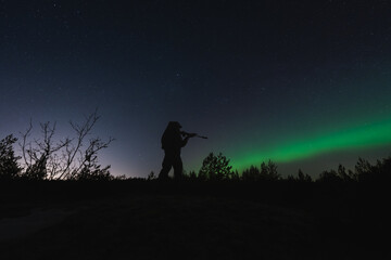 Silhouette of a military soldier with a rifle with a silencer and a night vision device against the...