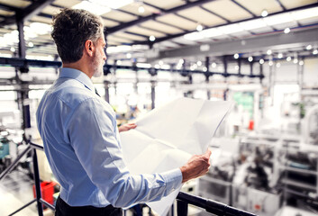 Portrait of project manager reading blueprint modern industrial factory. Manufacturing facility...