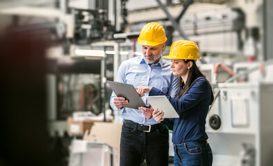 Two project managers standing in modern industrial factory. Manufacturing facility with robotics,...
