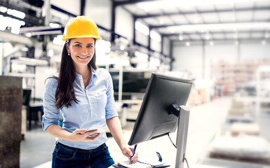 Female project manager standing by computrer in modern industrial factory. Manufacturing facility...