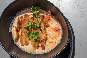 Crispy fried chicken slices on a spicy vegetable curry with coriander garnish in a black bowl, Asian meal, view from above