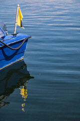 Stern of a blue boat with a yellow flag reflected in calm water with small waves, concept for...