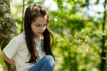 Portrait of a little girl in glasses sitting on a tree branch