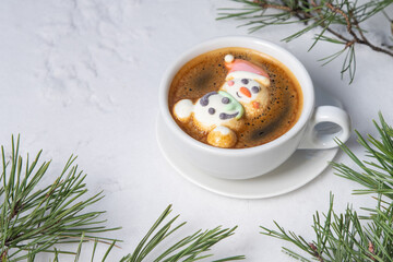 Cup of coffee with marshmallows. Marshmallow snowman in a Santa Claus hat. Winter drink in the snow. Christmas tree. Top view.