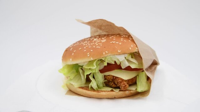 Close-up view of chickenburger with letuce salad in paper bag spinning against gray background. Bun covered with sesame seeds. Soft focus. Real time video. Fast food restaurant. Unhealthy eating theme