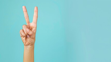 Hand showing two fingers in peace sign on light blue background
