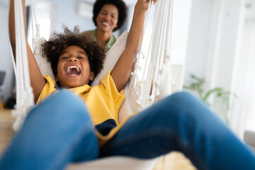 Playful African American little girl screams with joy as her mother pushes her on the swing at home.