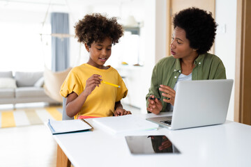 Supportive mother helping her daughter to finish her homework. She is explaining something while...