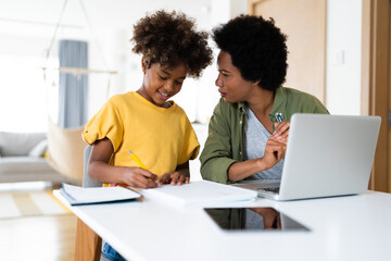 Caring mother helps her daughter to finish her homework. She talks while the girl writes in a...