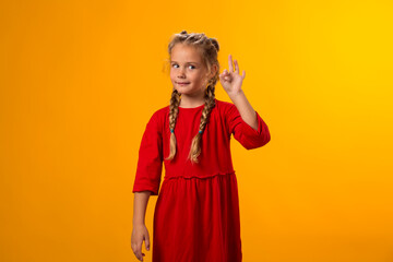 Smiling child girl looking through ok gesture over yellow background. Positive emotions concept