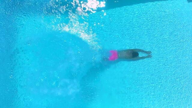 Aerial top slow motion view of a man diving into cool, blue swimming pool water, background of a summer concept