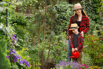 smiling mother gardener with child boy water the flowers from watering can in garden
