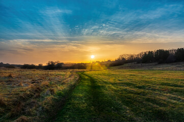 Obraz premium Landscape with the setting Sun over a meadow with a dirt country road. Picturesque nature and sunset