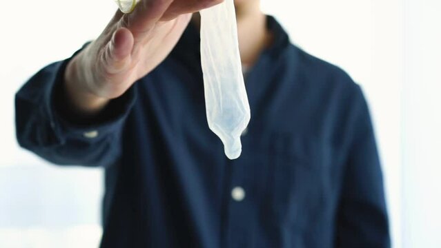 a man holds an unwrapped condom in his hands.
Method of contraception