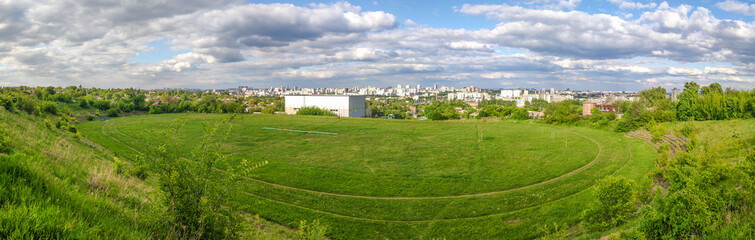 An old open-air athletics stadium overgrown with green grass, bushes and trees. Kharkiv city, Ukraine
