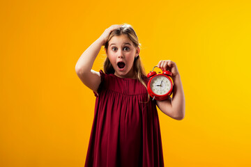 Surprised kid girl holding an alarm clock in hand. The concept of daily routine, school, deadlines,...