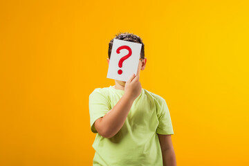 Kid boy holding question mark card in front of face. Education and curiosity concept