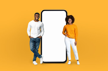 African American man and woman are standing side by side, looking at a blank phone screen. The man is holding the phone, while the woman is gesturing towards it.
