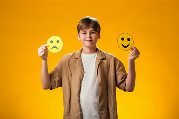 Boy holds emoticons with happy and sad emotions.