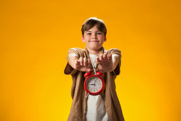 Boy holding alarm clock over yellow background. Time management concept