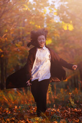 girl in black raincoat runs along the alley of city park the background of autumn maples, autumn toning, autumn background, selective focus