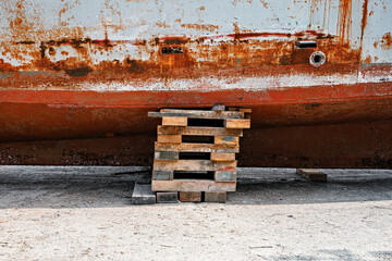 Weathered, rusty ship hull on wooden pallets on sandy ground, showcasing industrial decay