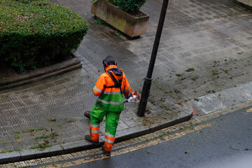 Man cutting the grass with a brush cutter wearing a mask and protective equipment in the street 