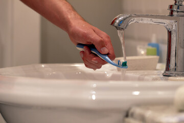 a man brings a toothbrush with toothpaste under running water from a tap in the bathroom,dentist...