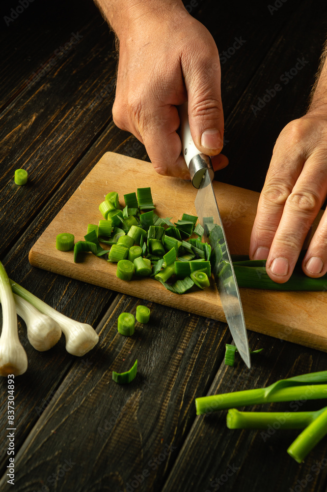 Wall mural A cook cuts green garlic on a cutting board with a knife to prepare a vegetarian dish. Place for advertising