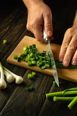 A cook cuts green garlic on a cutting board with a knife to prepare a vegetarian dish. Place for advertising