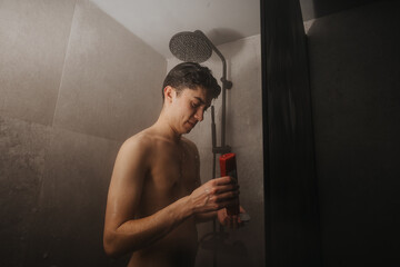 A man holding a shampoo bottle while taking a shower, exemplifying personal hygiene and self-care.