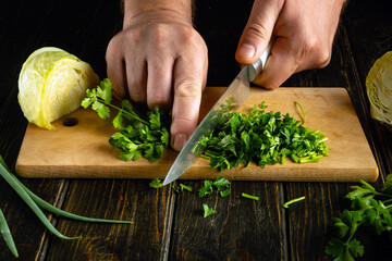 Chop parsley with a knife in the cook hand on a cutting board to prepare a vegetarian cabbage...