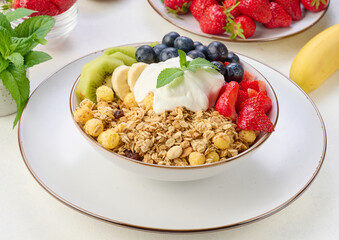 Granola with strawberries, kiwi, banana and blueberries in a round plate topped with yogurt on the table.